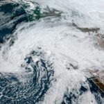 Satellite image showing a large swirling storm system with dense white clouds stretching across the western United States and the Pacific Ocean.