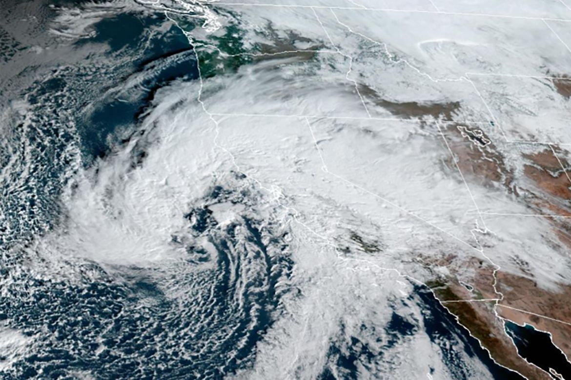 Satellite image showing a large swirling storm system with dense white clouds stretching across the western United States and the Pacific Ocean.